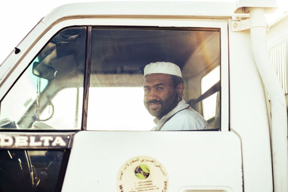 A Middle Eastern man smiles while sitting in a white truck indoors during the day.